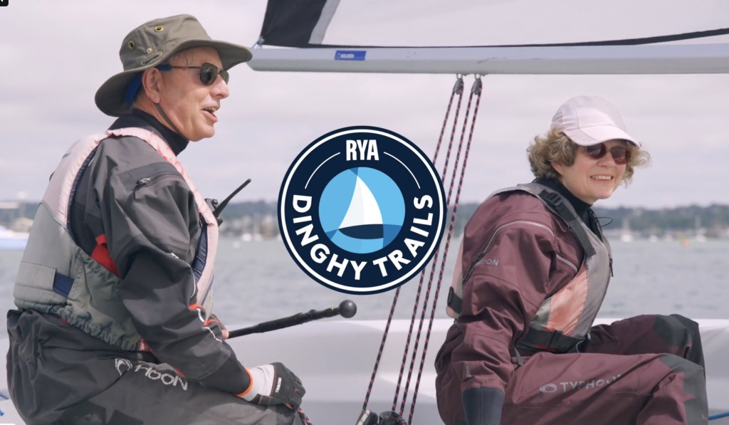 Two people sailing a dinghy behind the RYA Dinghy Trails logo.